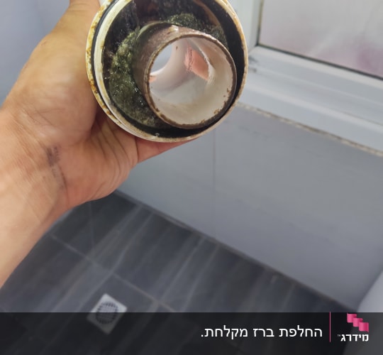 יד מחזיקה צינור עם לכלוך, חלון ברקע